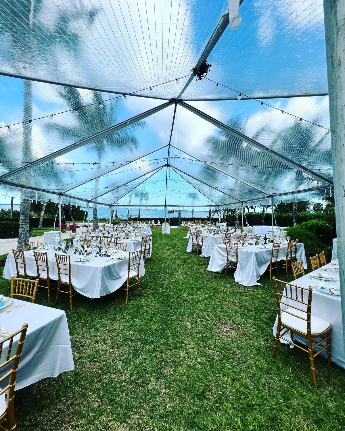 Clear-top event tent with round tables set for a wedding reception, waterfront view