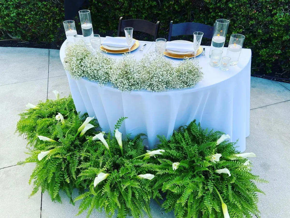 Bride and groom sweetheart table with white linens, ferns, and a floral runner